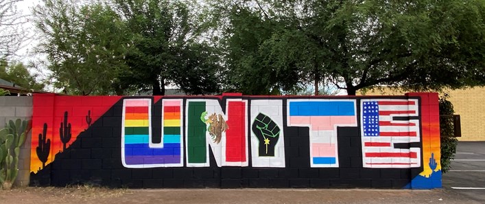 In brightly colored paint on a concrete brick wall is the word 'UNITE,' with each letter in colors representing a different identity or movement.