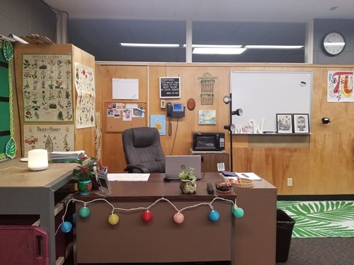 An image of WIniesdorffer's desk area: a variety of posters cover much of a wooden wall behind her desk, while a comfortable desk chair is pushed into the large brown desk in front of a silver laptop.