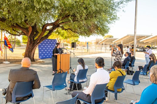 Arizona K12 Center Executive Director Dr. Kathy Wiebke, NBCT, speaks from a podium outside Encanto Elementary School to media on blue plastic chairs about the creation of the Arizona Teacher Residency.