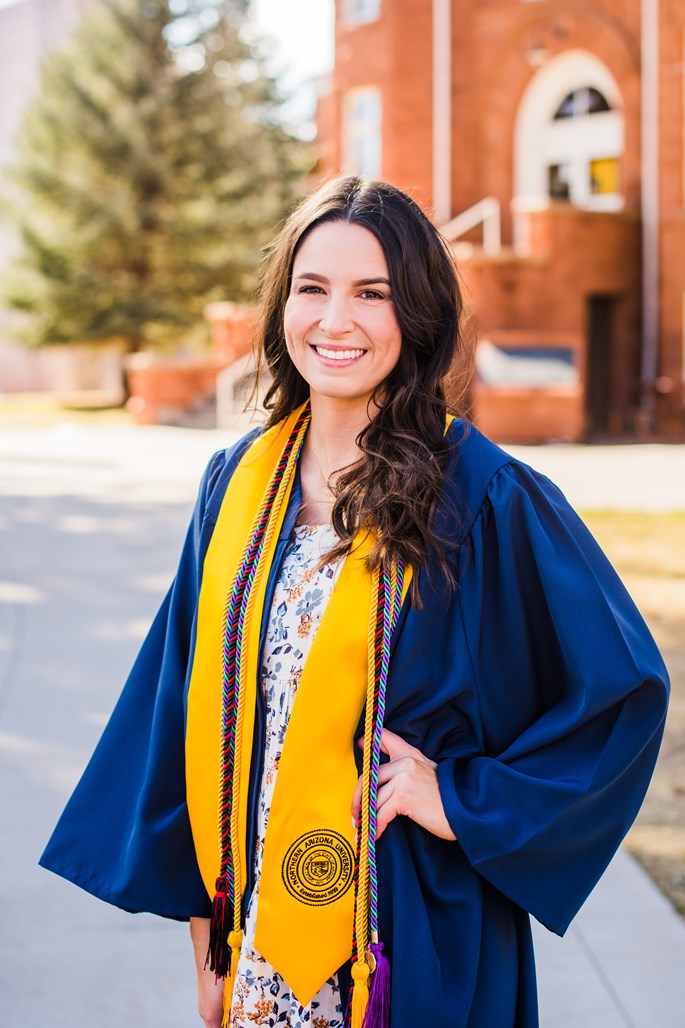 Katee Hurst stands on NAU's campus dressed in her graduation robe and garb.