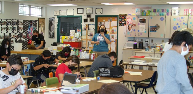 Art teacher Candace Green gives directors to a class of students from the side of the classroom. Students are listening while working on their painting projects.